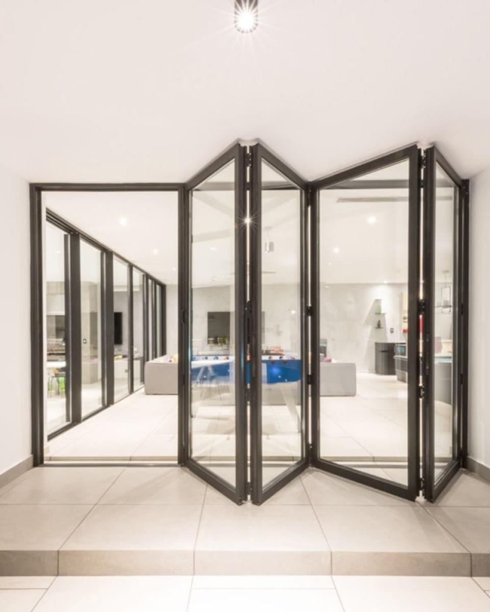 Modern bifold glass doors with dark frames opening to reveal contemporary home interior with pool view